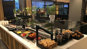 Un bufé con diversas opciones de comida, entre ellas frutas, pasteles y salsas.