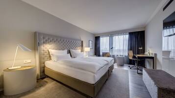 A modern hotel room with a large bed, a desk, and a comfortable seating area.