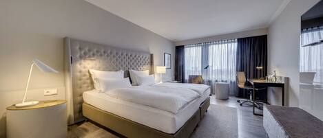 A modern hotel room with a large bed, a desk, and a comfortable seating area.