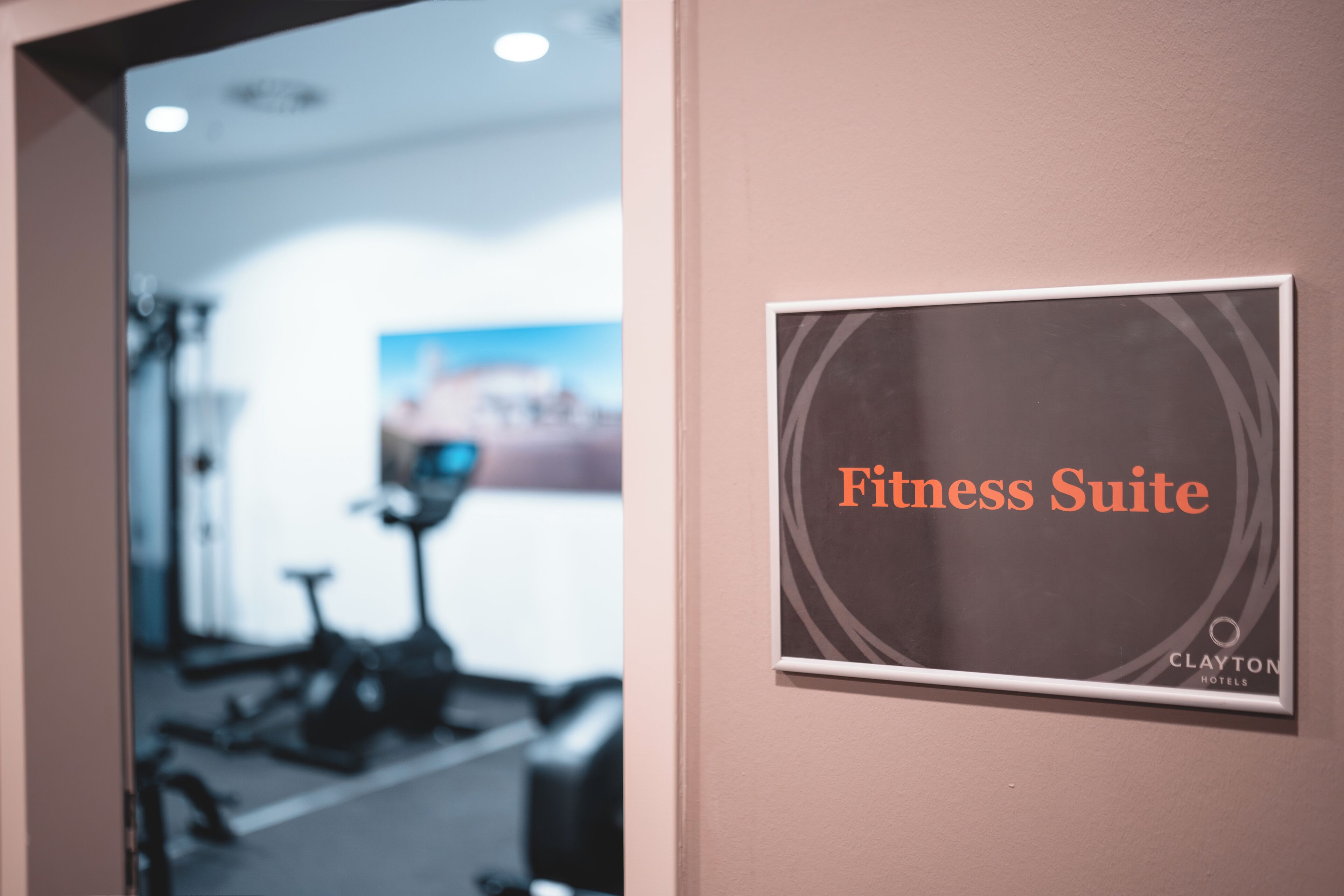 A sign indicating a Fitness Suite in a hotel, with a blurred background of gym equipment.