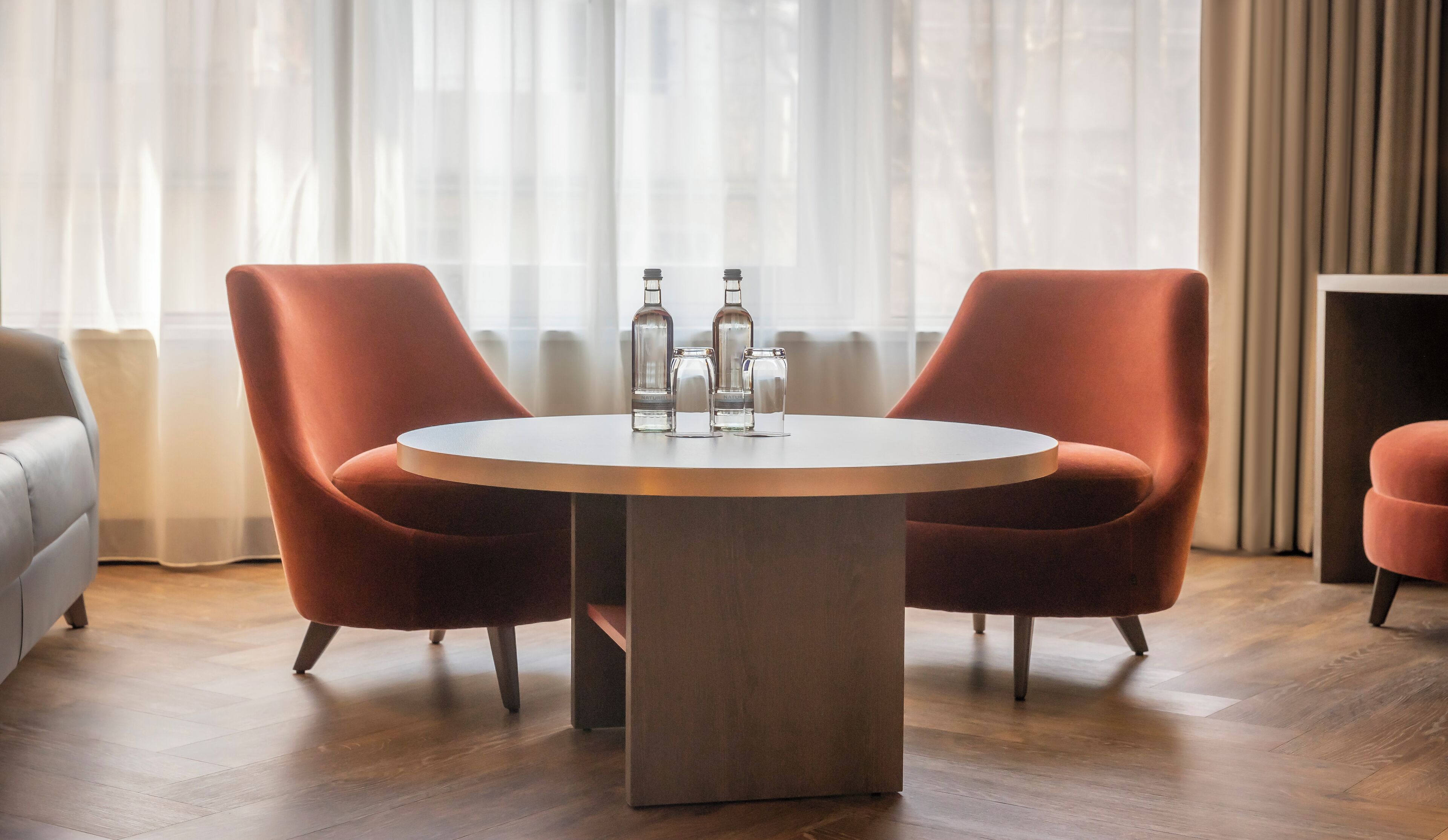 A modern room with a round table, two orange chairs, and three bottles on the table.