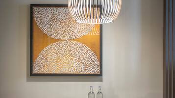 A dining area with a round table, orange chairs, a modern pendant light, and a framed abstract artwork on the wall.