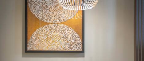 Un coin repas avec une table ronde, des chaises orange, un luminaire suspendu moderne et une œuvre d’art abstraite encadrée accrochée au mur.