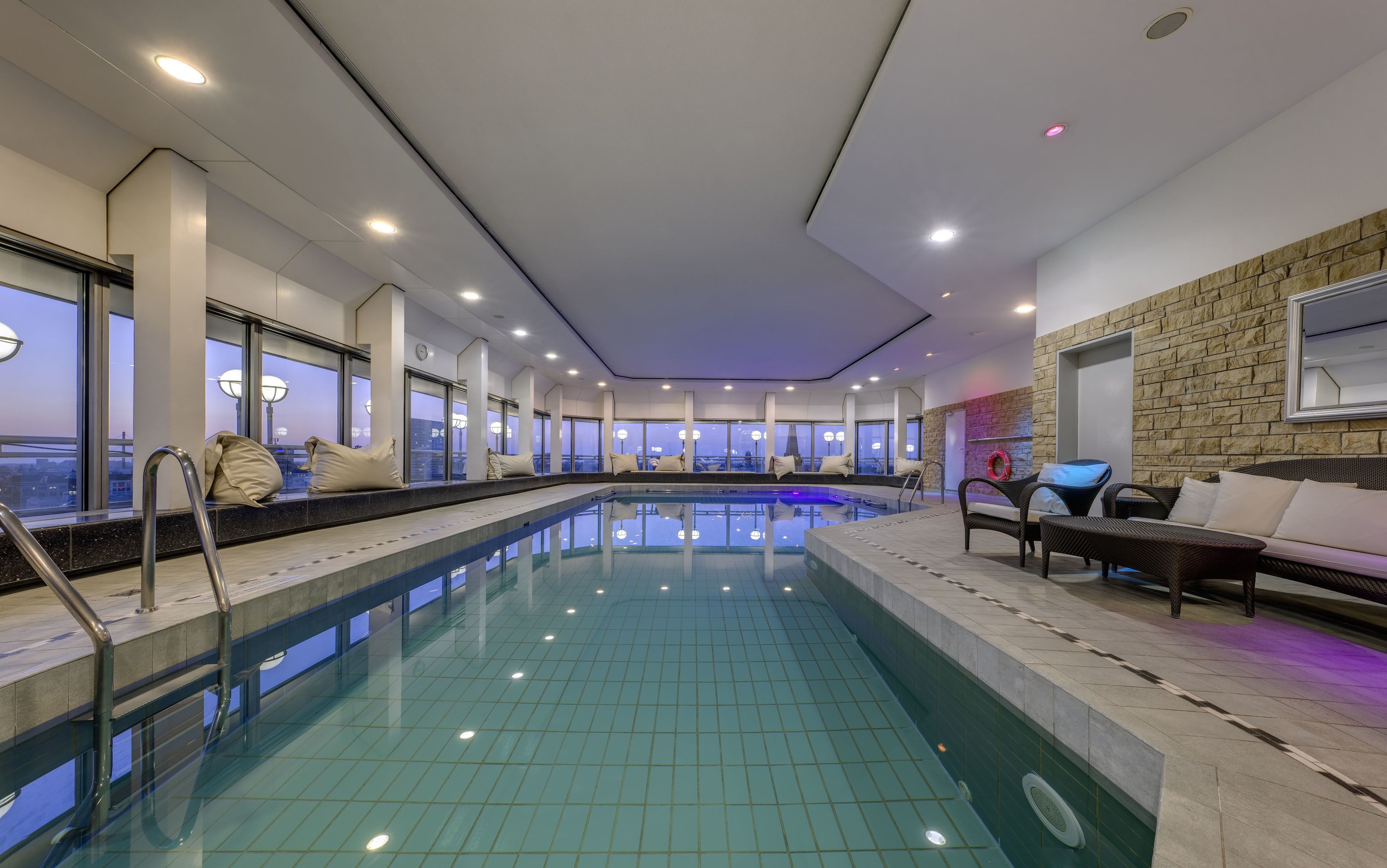 Una piscina interior moderna con zonas de estar y ventanas amplias.