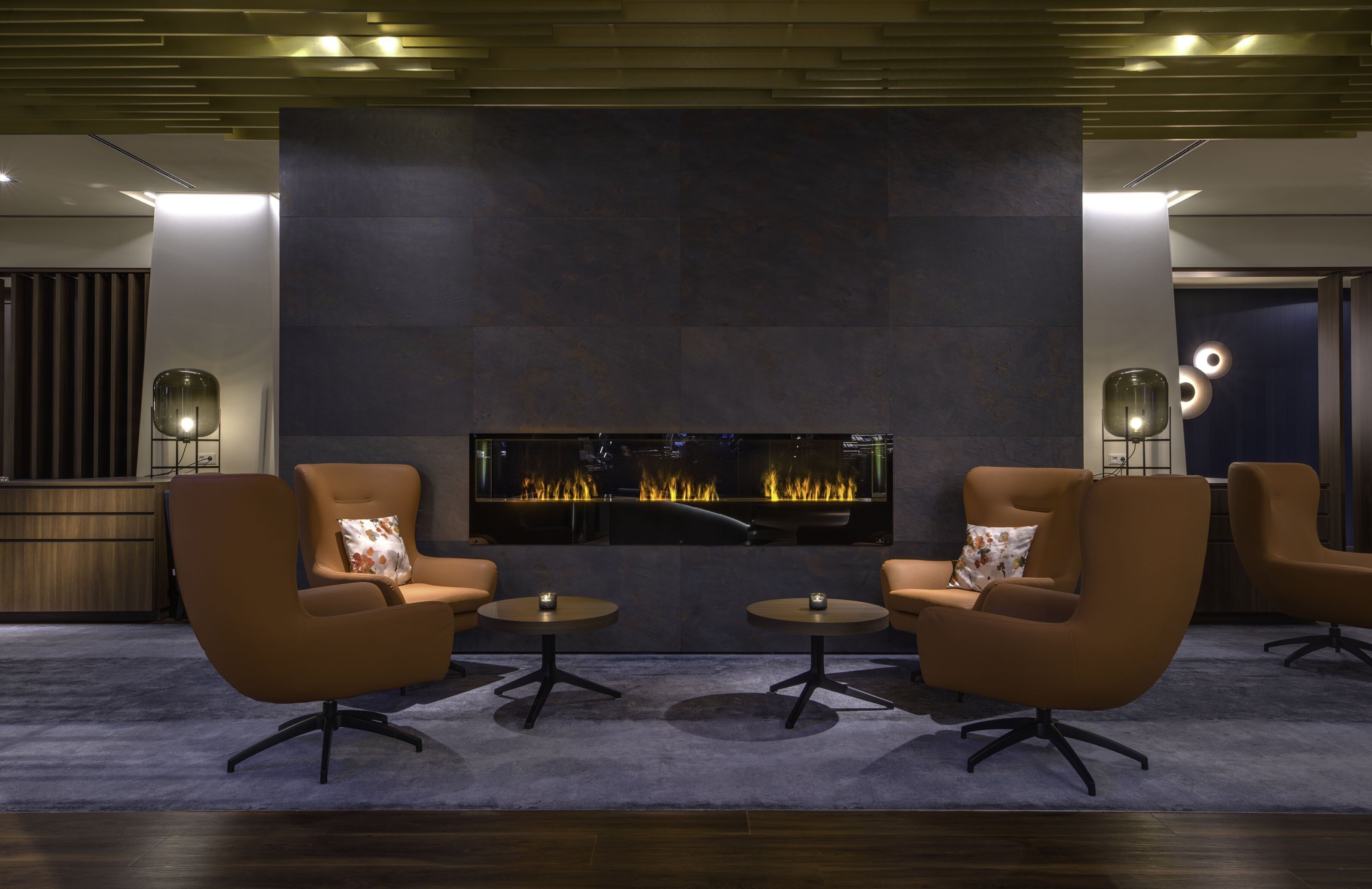 A modern lounge with a fireplace, leather armchairs, and round tables.