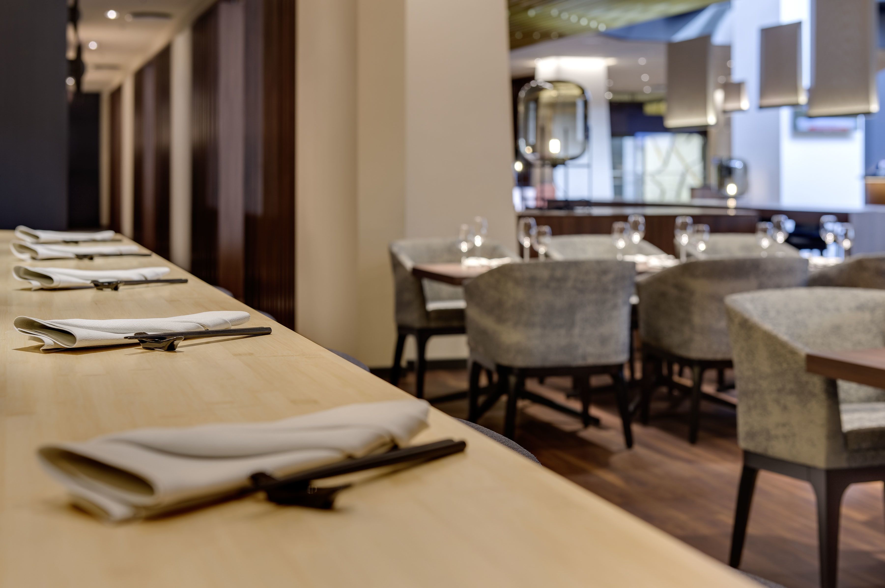 A restaurant with a long counter, neatly folded napkins, and chairs arranged for dining.