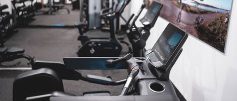 A gym with exercise equipment, a wall-mounted TV, and a poster of a scenic road.