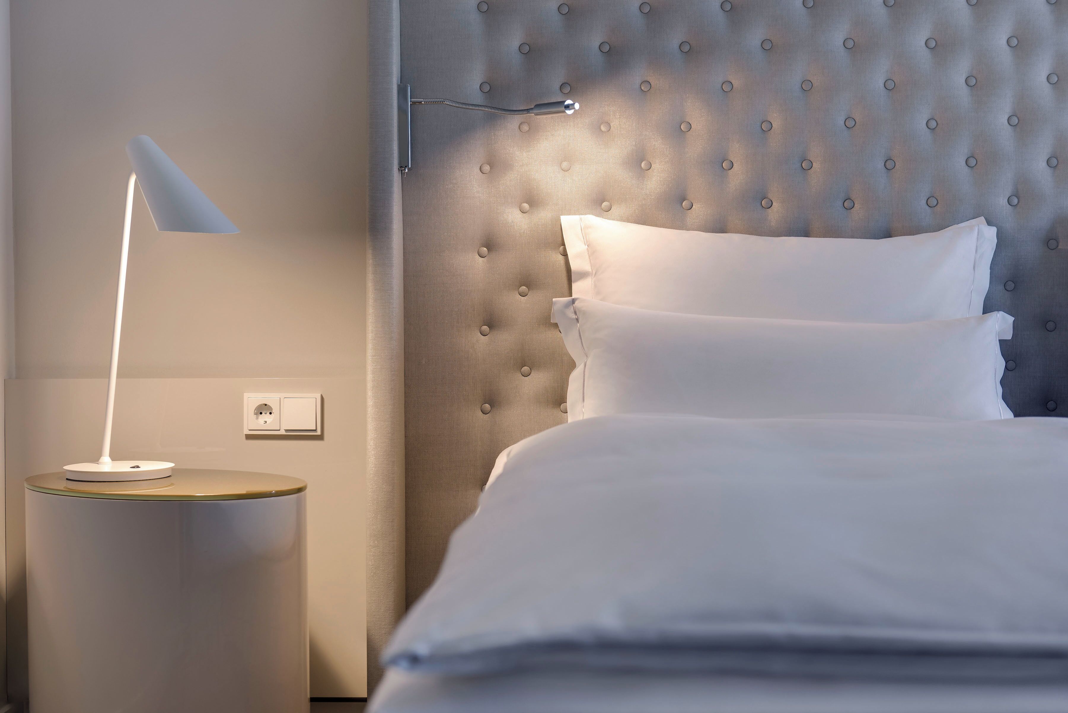 A neatly made bed with white linens and a tufted headboard.