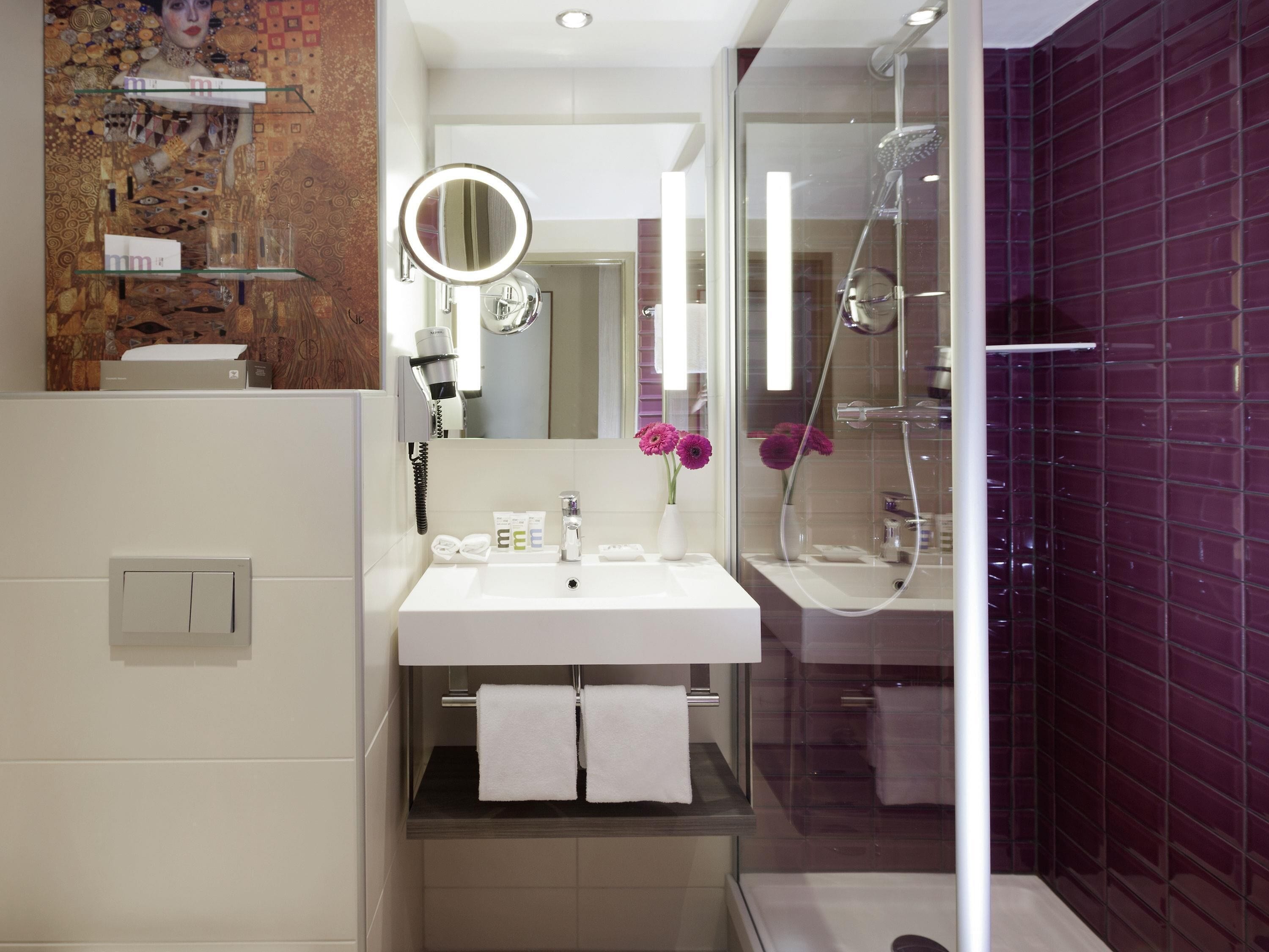 Ein modernes Badezimmer mit einem weißen Waschbecken, einem Spiegel, einer Dusche und violett gefliesten Wänden.