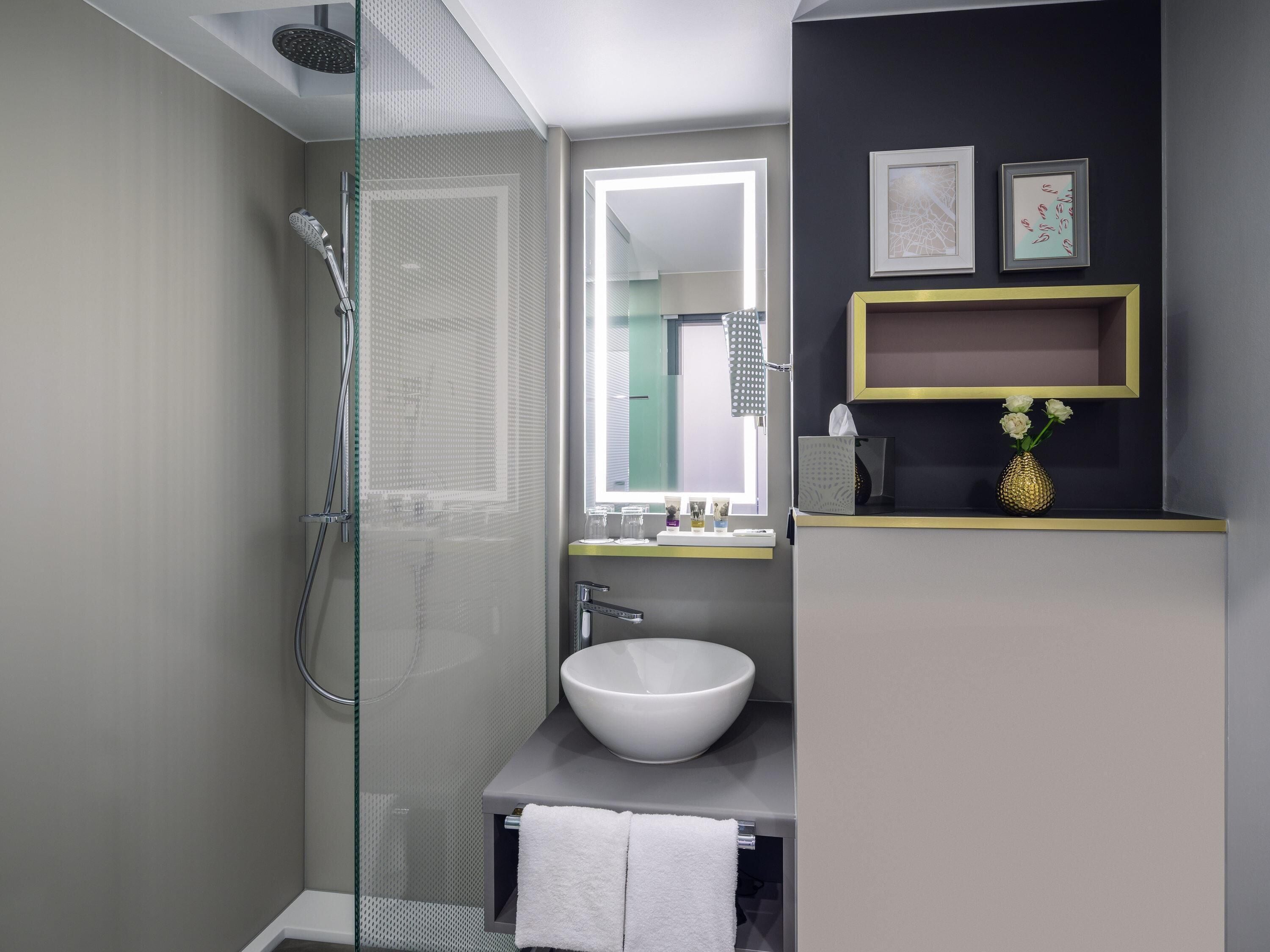 A modern bathroom with a glass-enclosed shower, a white sink, and a vanity with a mirror.