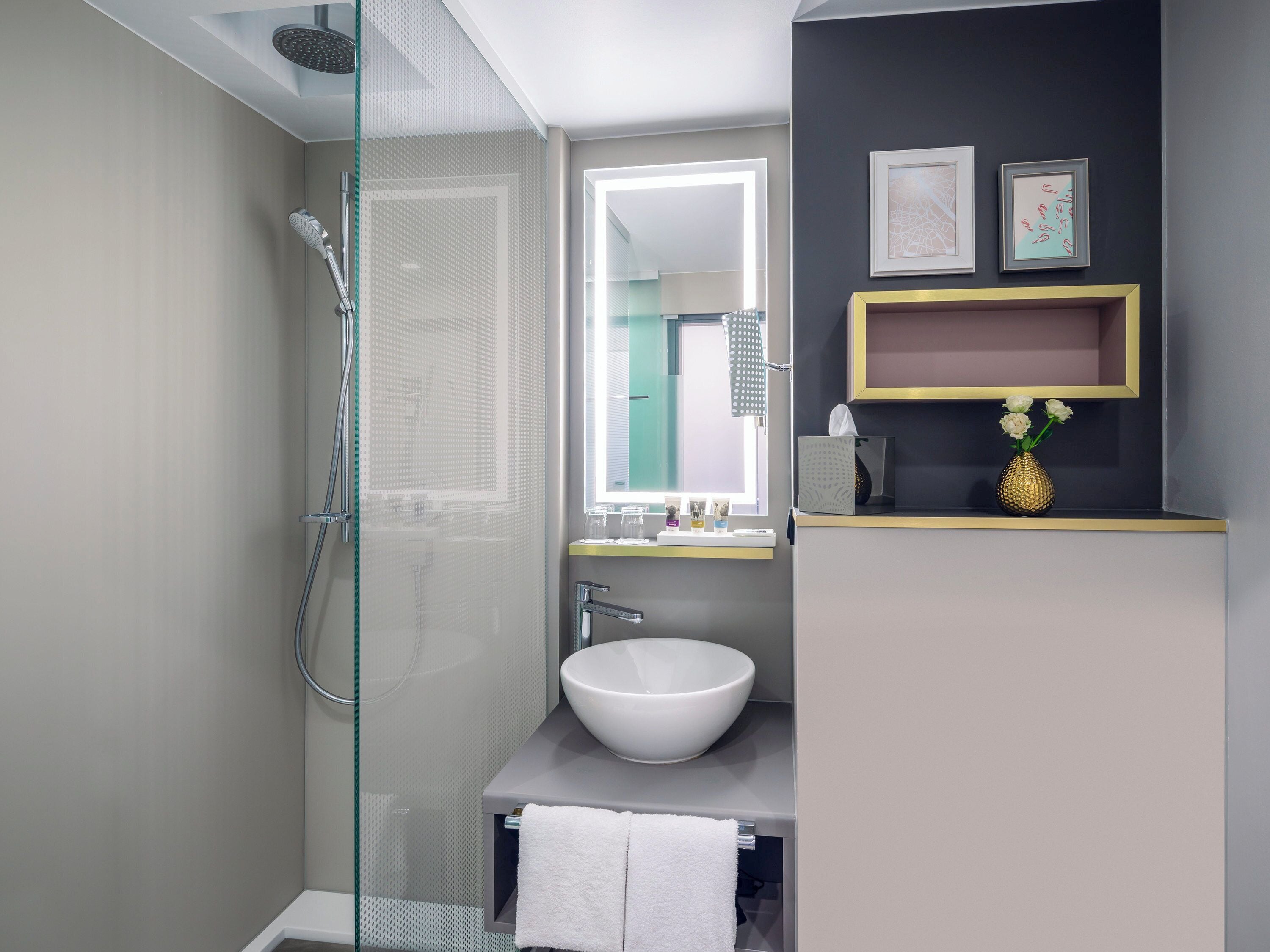 A modern bathroom with a glass shower enclosure, a white sink, and a vanity with a mirror.