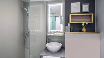 A modern bathroom with a glass shower enclosure, a white sink, and a vanity with a mirror.