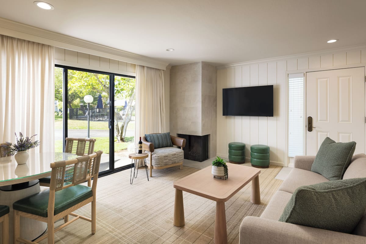 A spacious living room with a glass door leading to a patio, a flat-screen TV mounted on the wall, and a comfortable seating area with a sofa and chairs.
