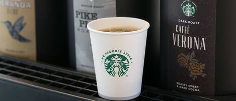 Una taza de Starbucks en un estante con dos cafeteras que dicen Pike Place Roast y Cafe Verona.