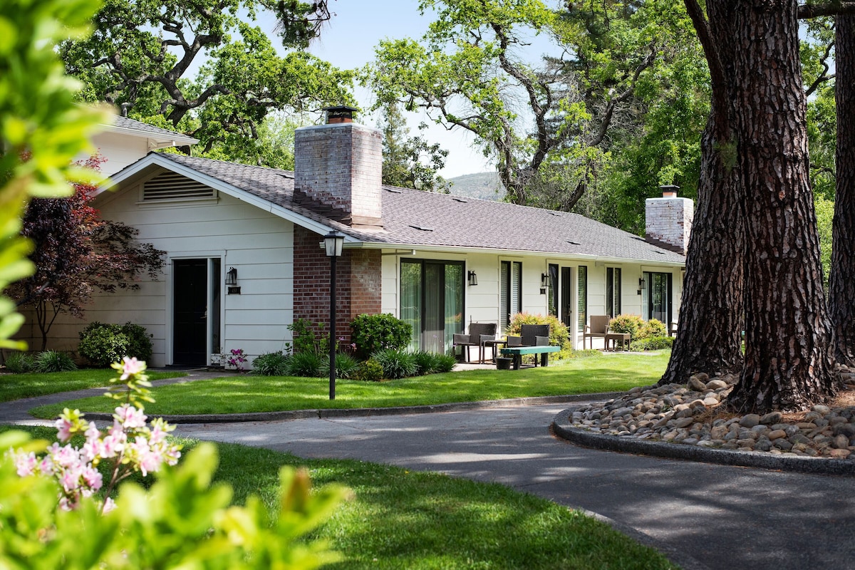 A two-story house with a brick chimney, a front porch with a bench, and a well-maintained lawn.