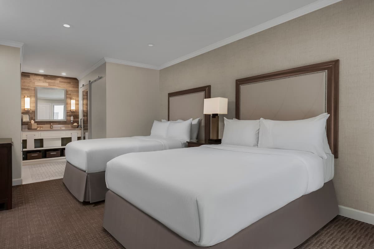 A hotel room with two beds, a bathroom, and a large mirror.