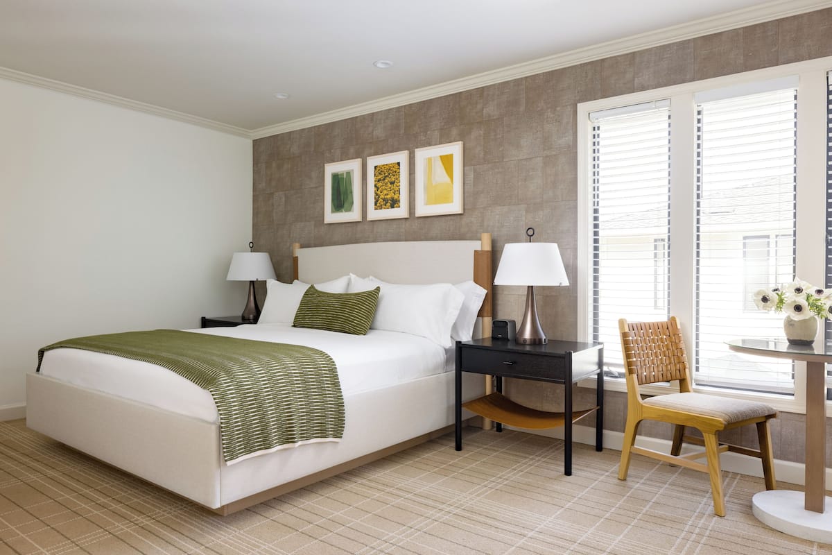 A hotel room with a large bed, bedside tables, a chair, and a window with blinds.