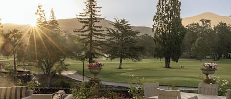 A patio with wicker furniture, a table, and chairs, overlooking a golf course with a mountain in the background.
