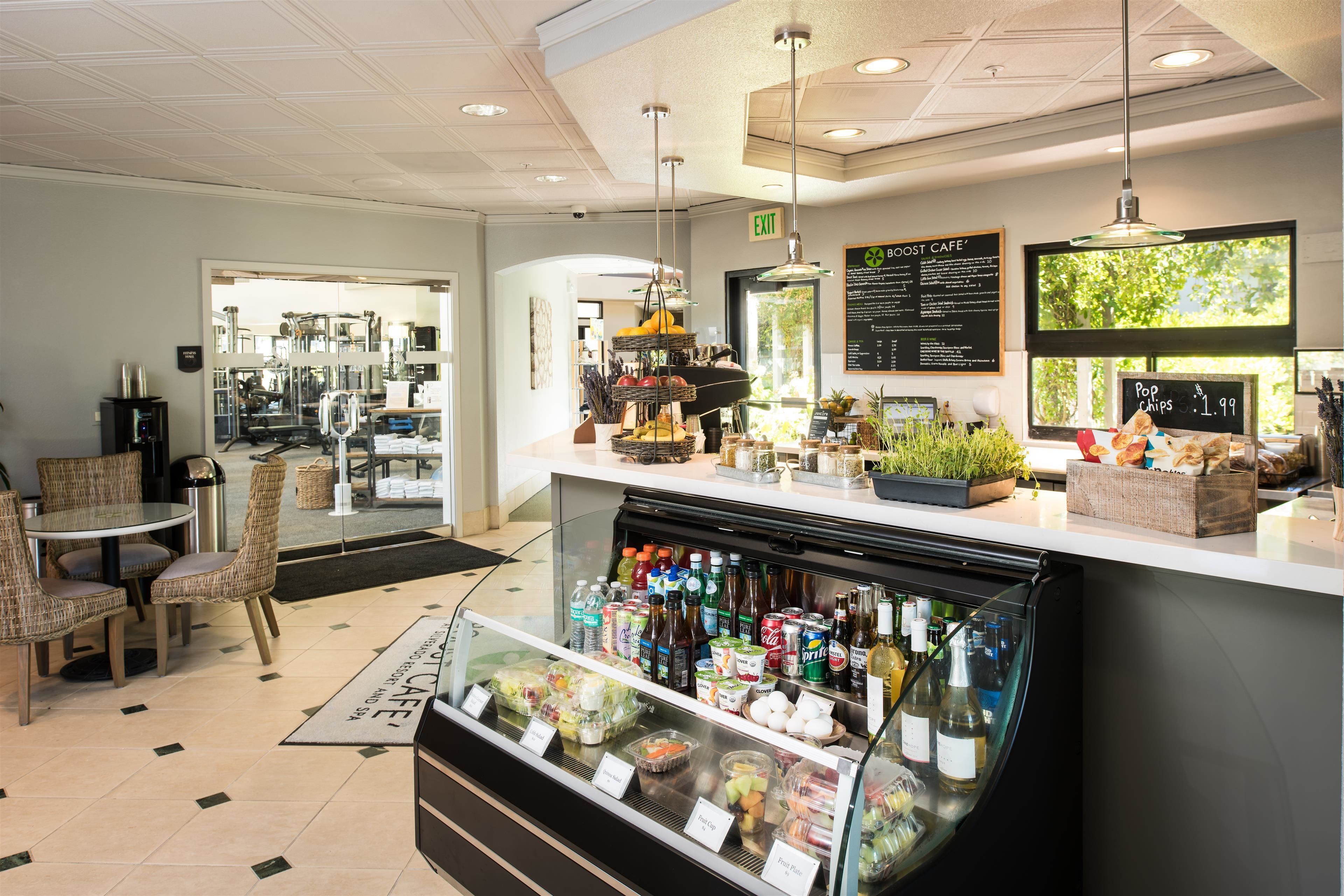 A cafe with a glass display case filled with beverages and snacks, wicker chairs, and a menu board.