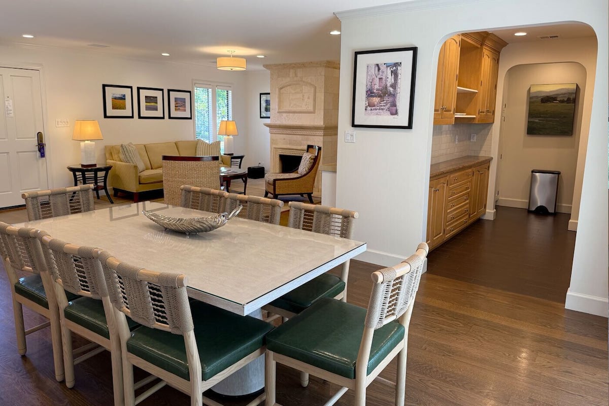 A dining area with a round table and chairs, a kitchen with wooden cabinets, and framed artwork on the walls.