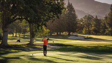 A golf course with a golfer taking a shot, surrounded by trees and a mountain in the background.
