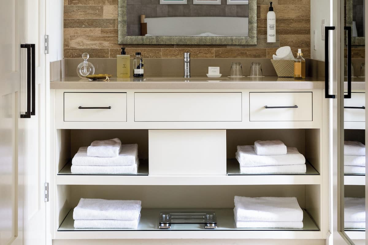 A modern bathroom with a large mirror, built-in shelves for towels, and a stone backsplash.