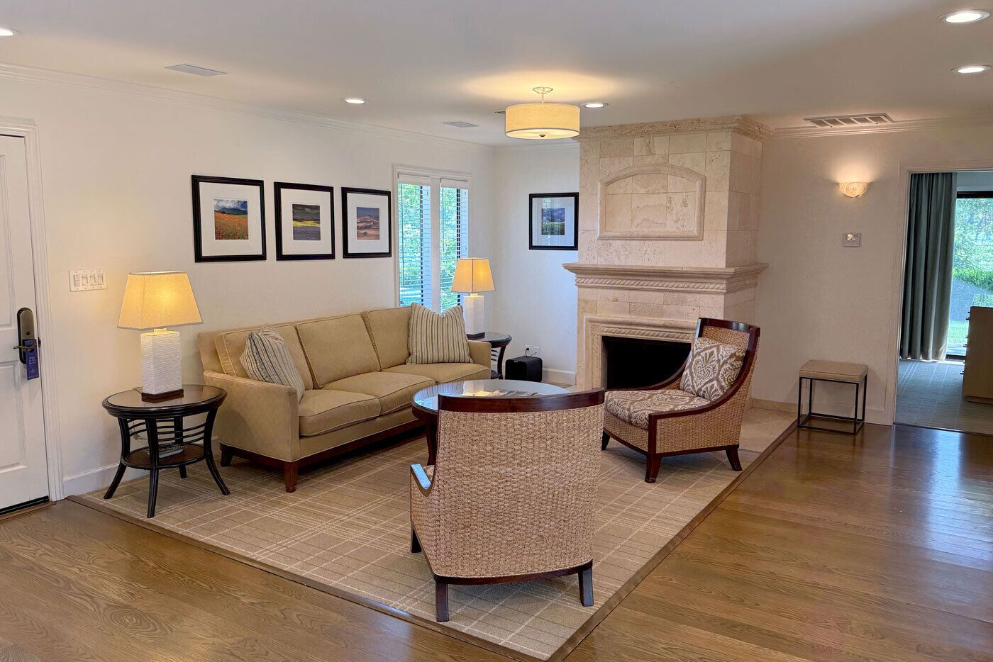 Un salon avec un canapé beige, deux fauteuils, une table basse, une cheminée et des tableaux encadrés accrochés au mur.