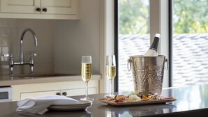 Una cocina con ventana, un lavabo y una mesa con un plato de comida y dos copas de vino.