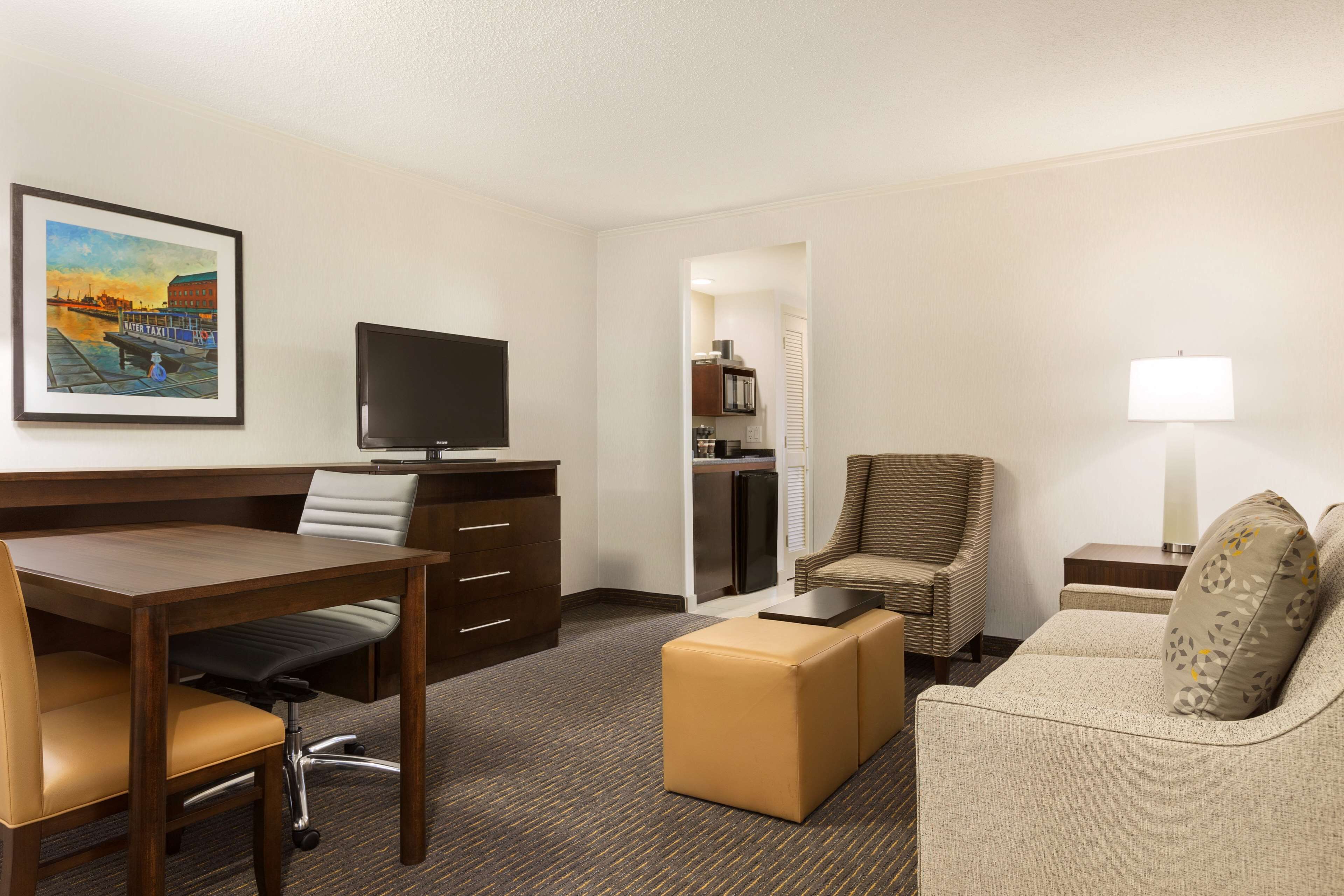 A hotel room with a wooden desk, a television, a sofa, a chair, and a small table with a lamp.