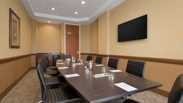 Un salón de conferencias con una mesa larga, sillas negras, un televisor de pantalla plana y una puerta al fondo.