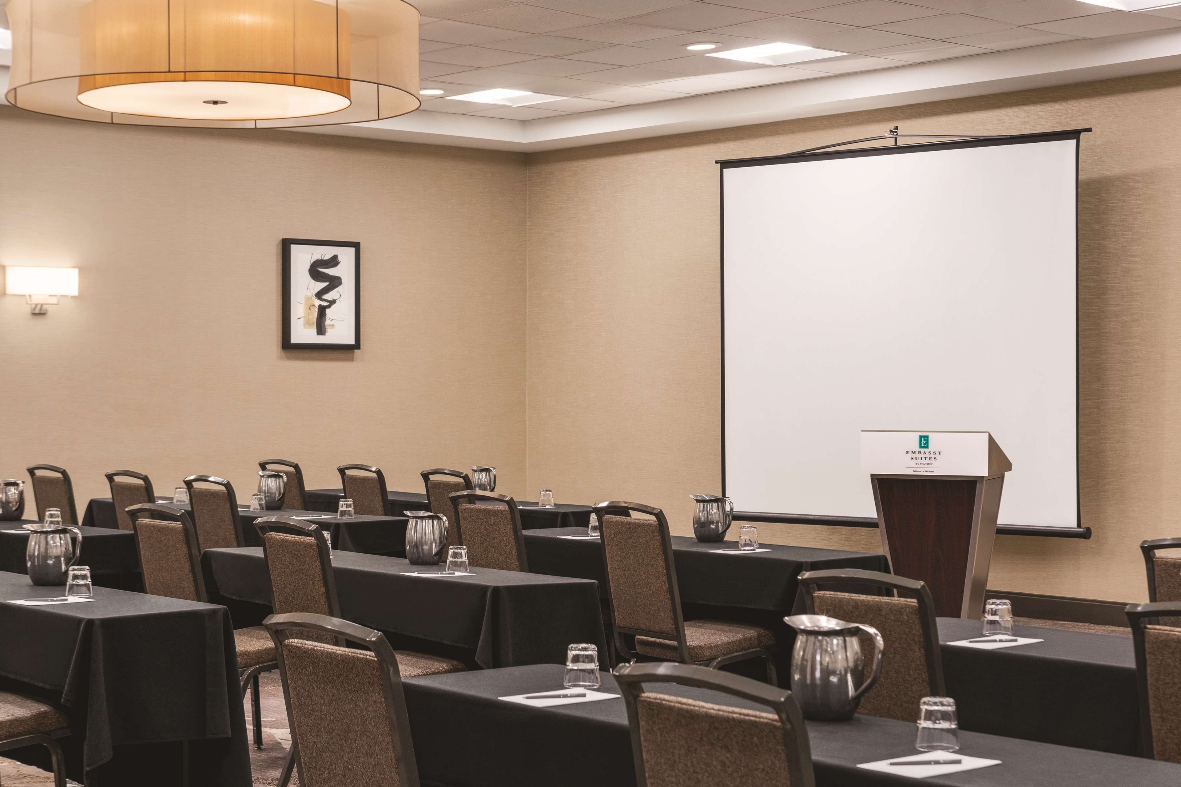 A conference room with tables, chairs, a projector screen, and a podium.