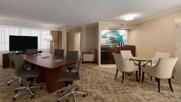 Habitación de hotel con escritorio, sillas de oficina, televisión, zona de cocina y comedor.