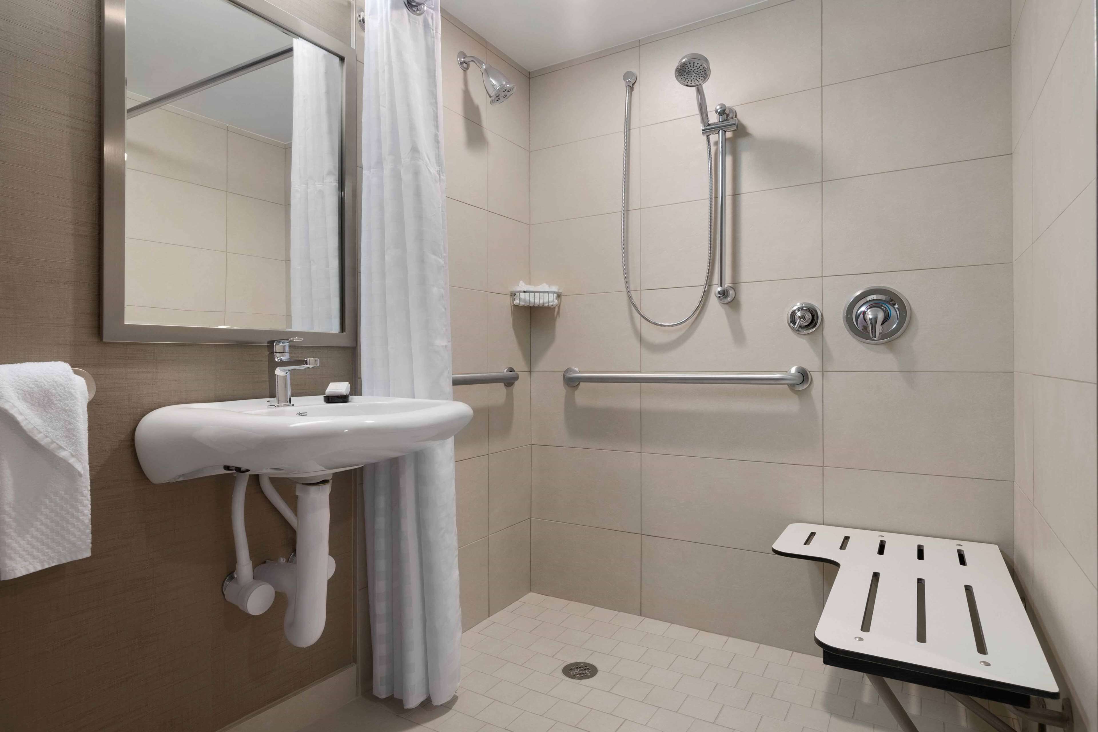 A modern bathroom with a sink, mirror, shower, and grab bar.