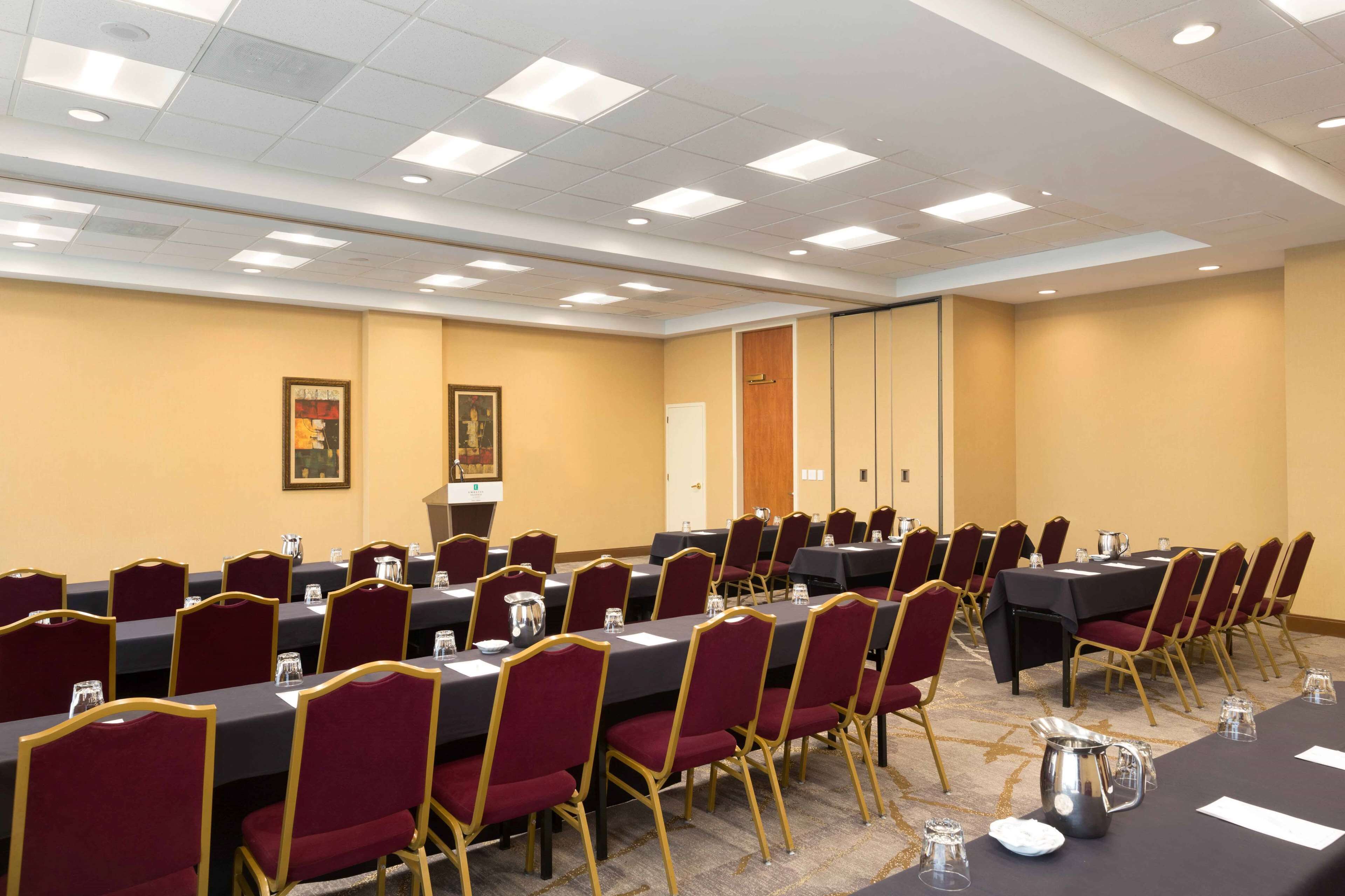 Un salón de conferencias con varias mesas y sillas, equipado con jarras de agua y vasos.