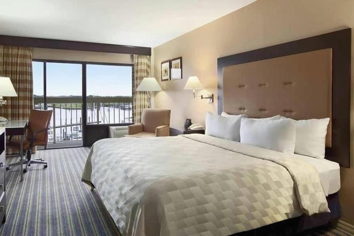 A hotel room with a large bed, a desk, a chair, and a view of the outdoors.