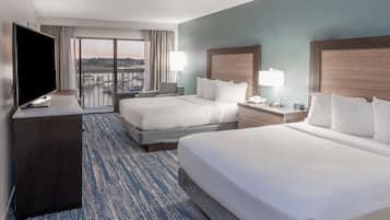 Habitación de hotel con dos camas, televisión, escritorio y balcón con vista a la ciudad.
