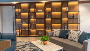 A modern living room with a sectional sofa, a coffee table, and a decorative wall unit with shelves. - DoubleTree by Hilton New Bern Riverfront (New Bern)