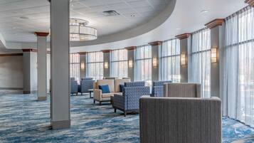 A spacious lobby with a blue carpet, several seating areas, and large windows with curtains.