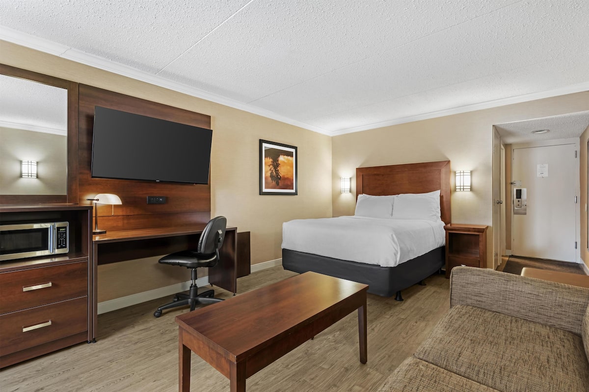 A hotel room with a bed, desk, chair, TV, and a small table.