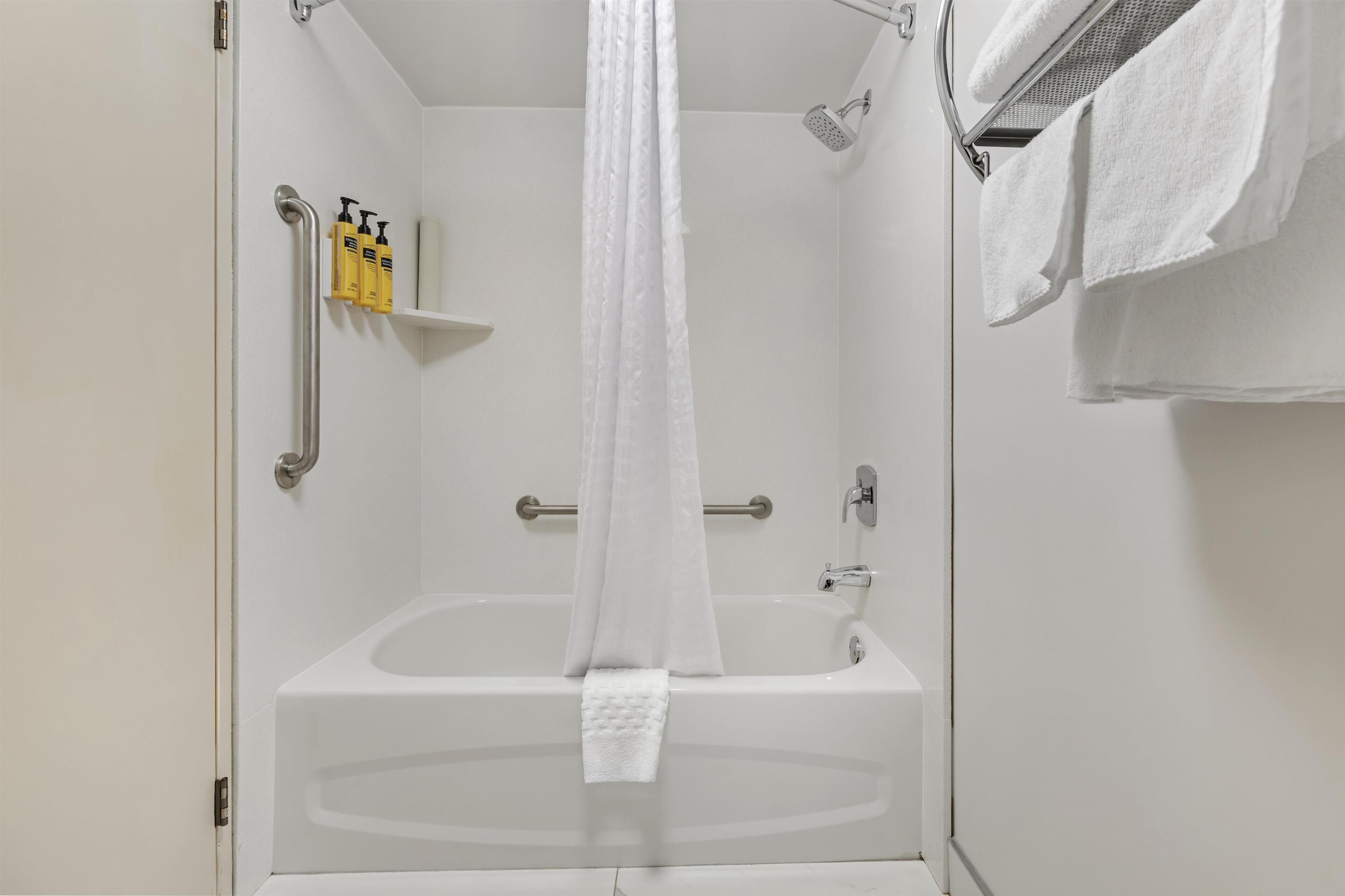 A bathroom with a bathtub, a shower, a towel rack, and a shelf with toiletries.