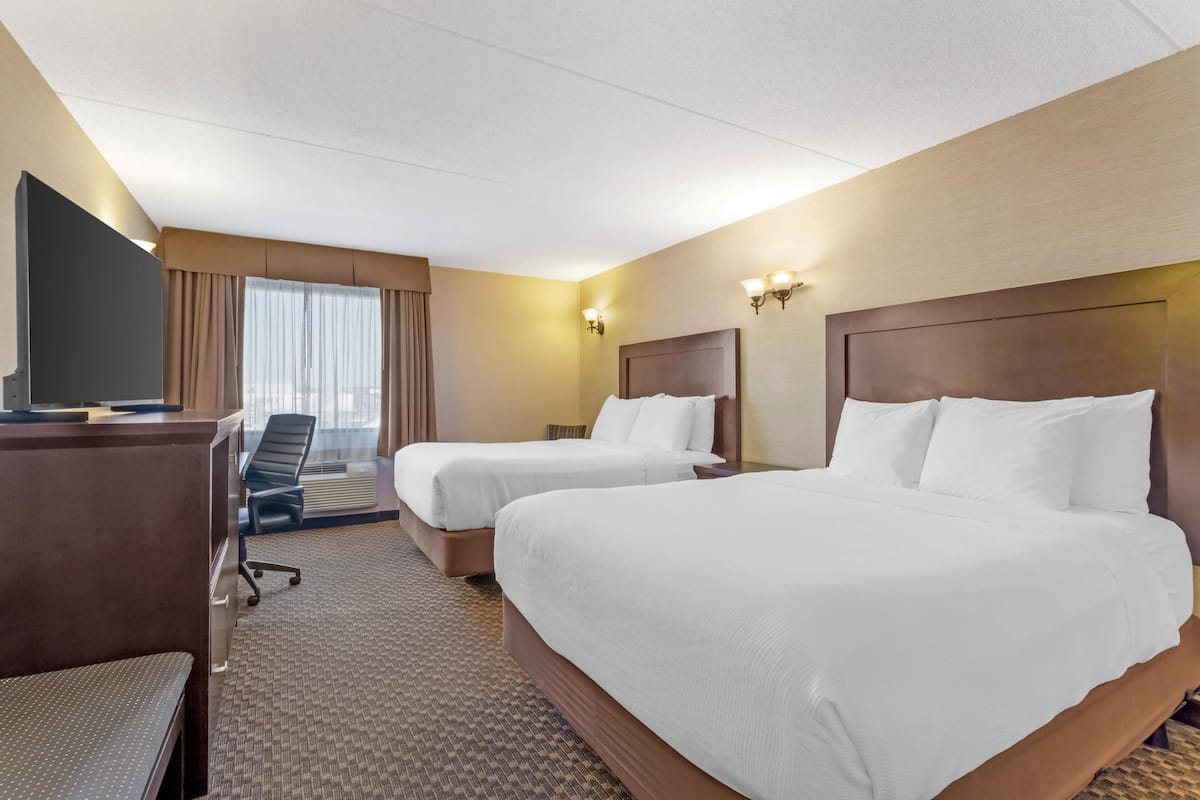 A hotel room with two beds, a desk, a chair, and a television.
