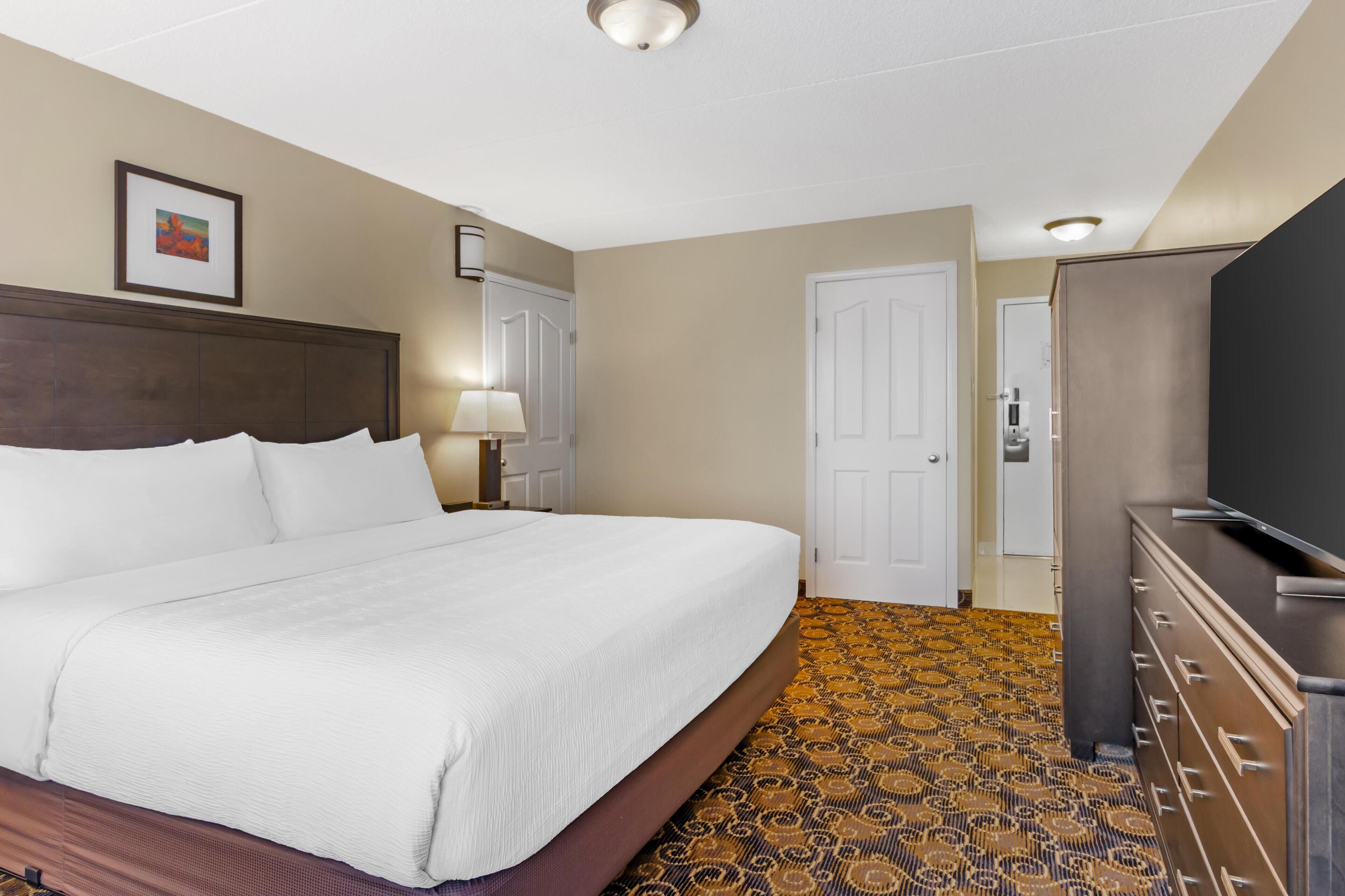 A hotel room with a large bed, a dresser, a television, and a patterned carpet.