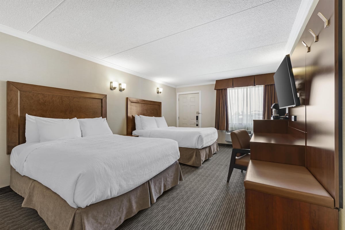 A hotel room with two beds, a desk, a TV, and a door.