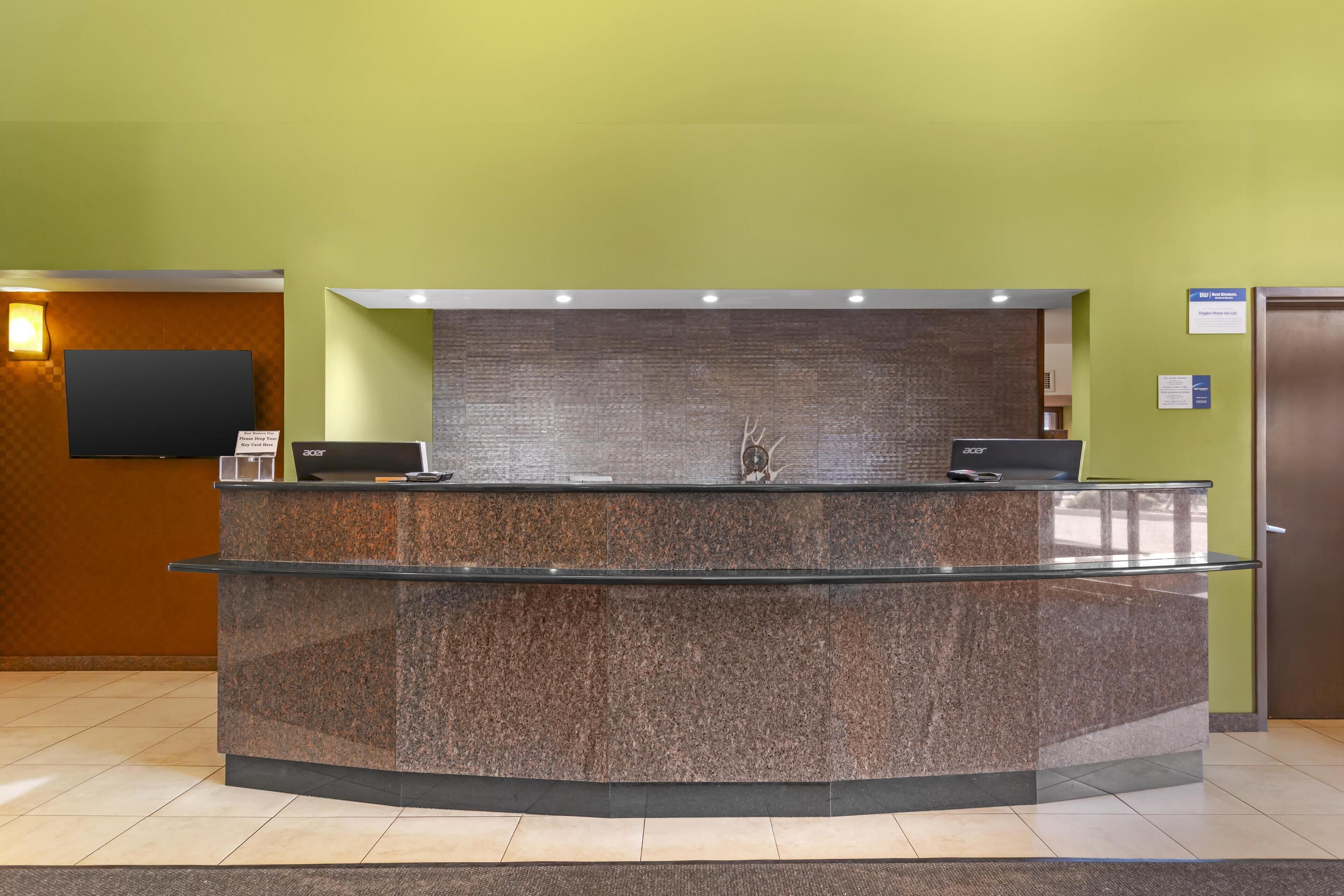 A reception desk with a glass top, a flat-screen TV mounted on the wall, and a sign indicating a key card drop area.