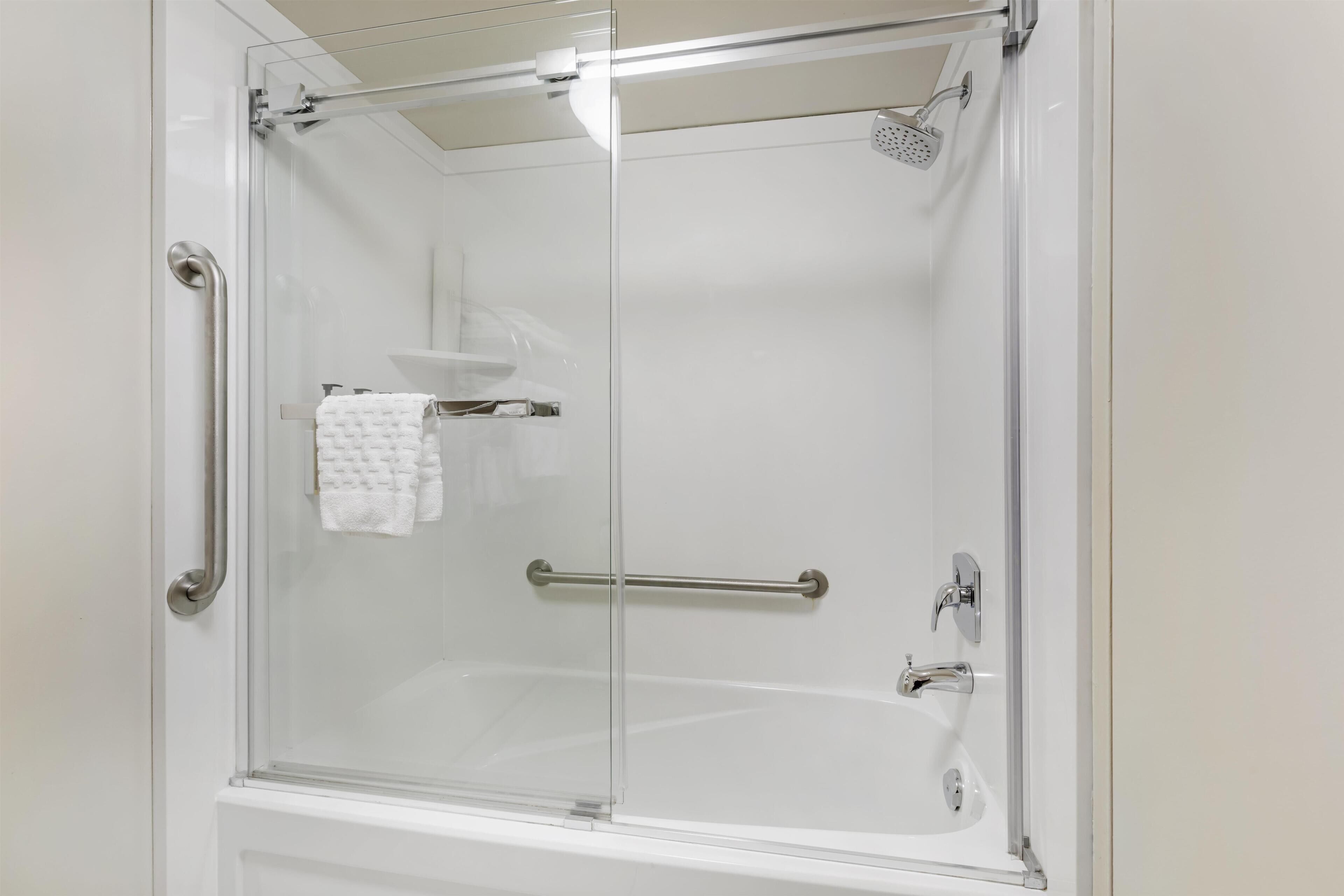 A glass-enclosed shower with a handheld showerhead, a towel rack, and a grab bar.