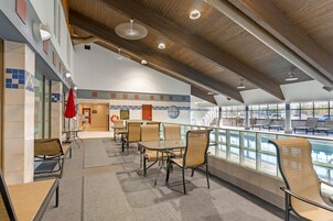 Amplio espacio interior con varias mesas y sillas, vista a la piscina y pared de azulejos con diseños geométricos.