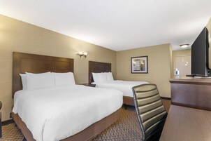 Habitación de hotel con dos camas, un escritorio, una silla y un televisor.