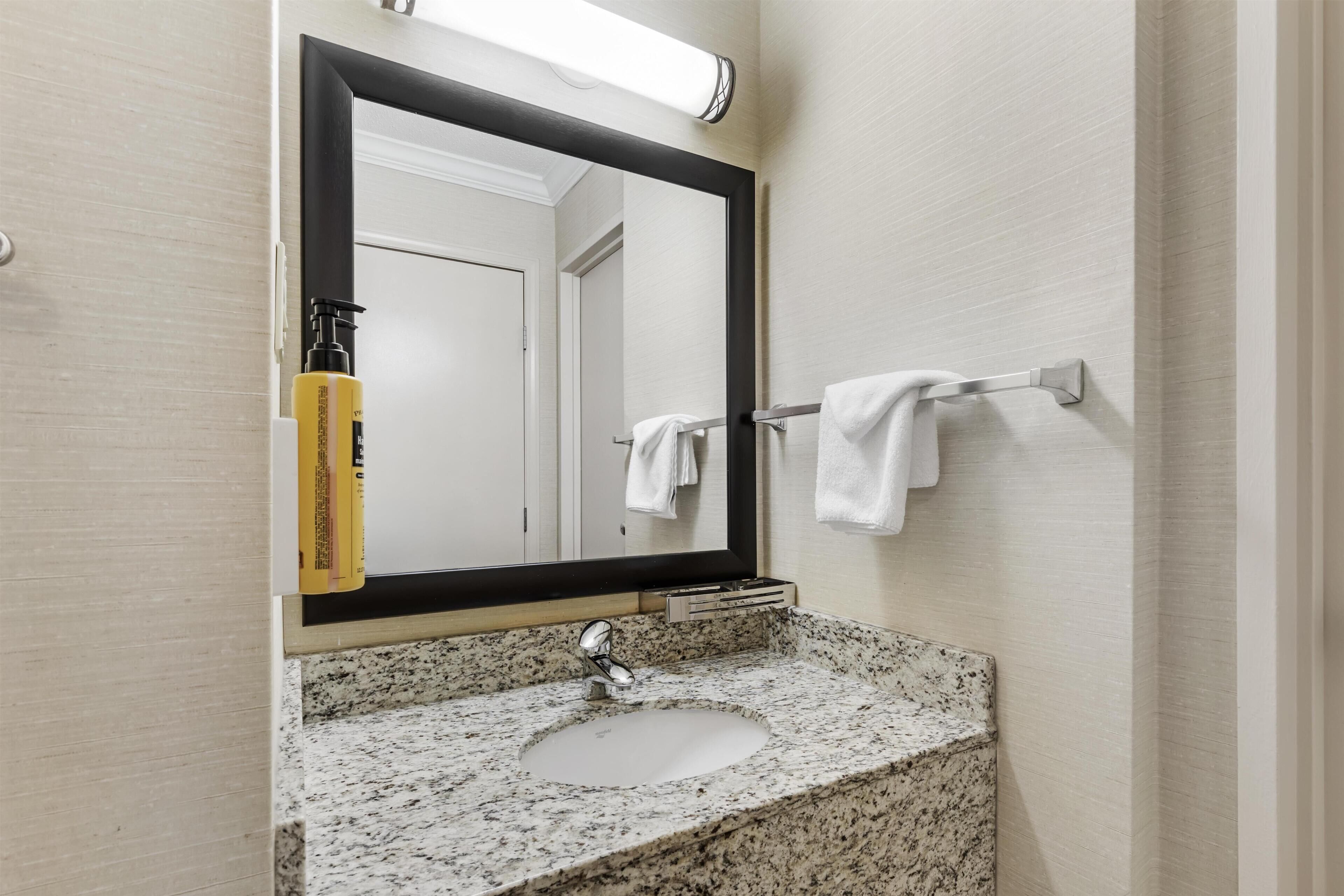 A bathroom with a granite countertop, a sink, a mirror, and a towel rack.