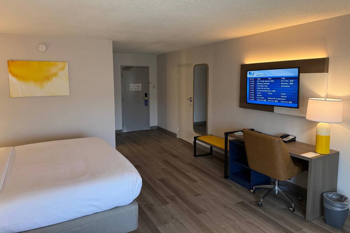 A hotel room with a bed, desk, chair, and a television displaying a menu.
