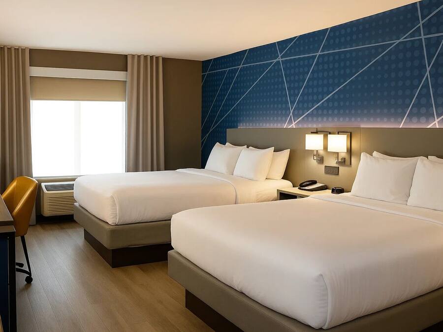 Een hotelkamer met twee bedden, een bureau, een stoel en een groot raam met gordijnen.
